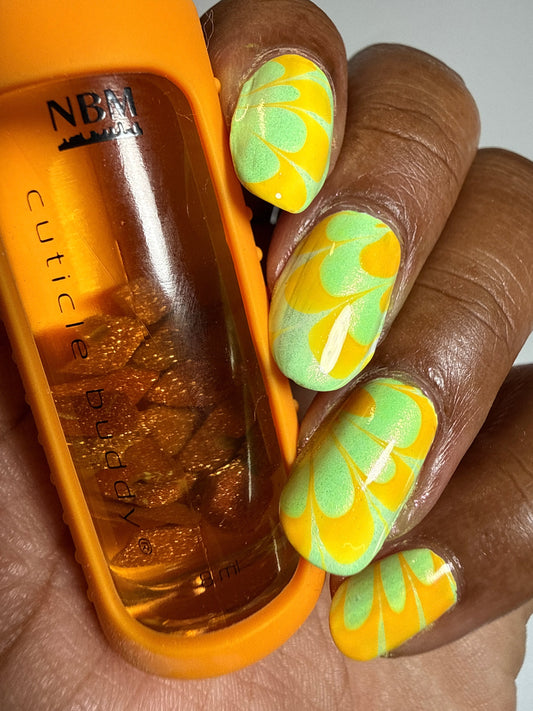 a brown hand holding an orange cuticle oil called cuticle buddy from www.shopnbm.com